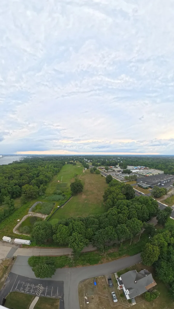 Aerial drone view over Silver Spring Golf Course in Riverside RI showing green fairways and grounds framed by trees with Narragansett Bay in the distance