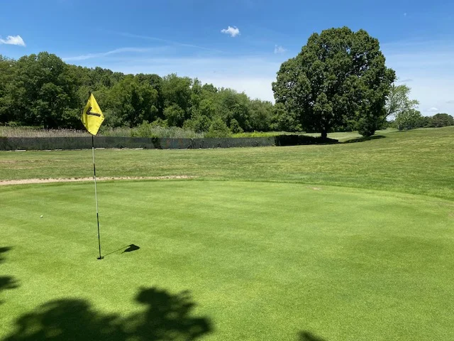 Yellow pin flag on a freshly mown green with a wide summer fairway at Silver Spring Golf Club Riverside RI